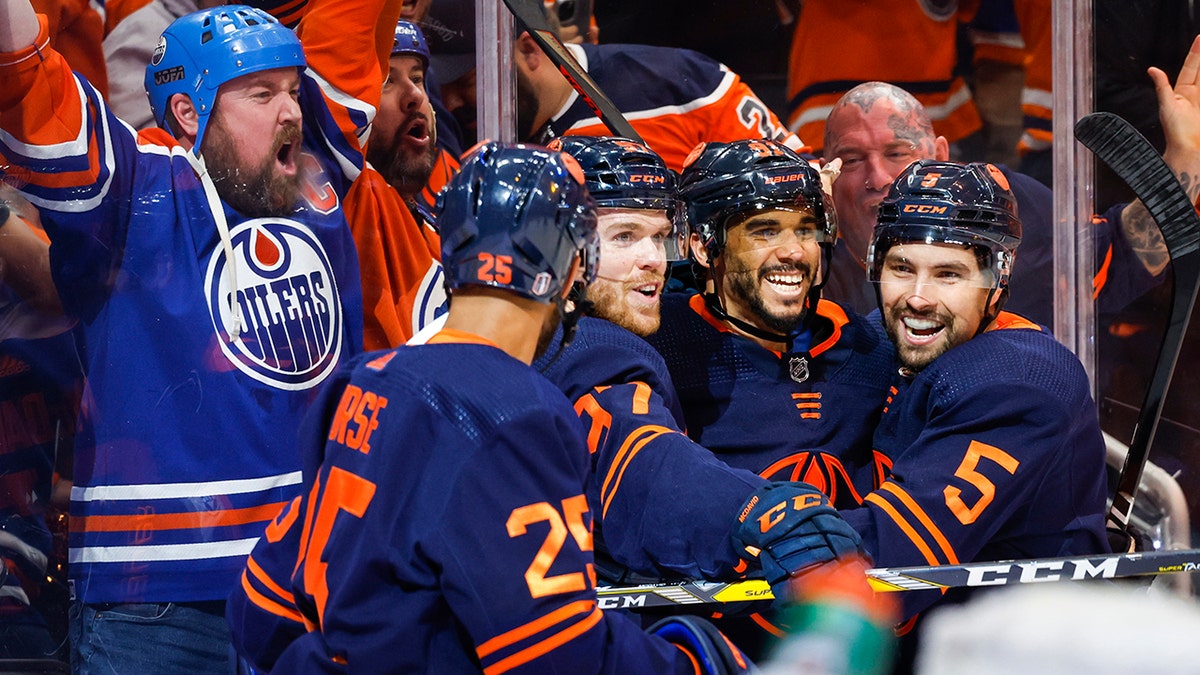 Oilers, wearing blue, orange and white jerseys, celebrate a goal