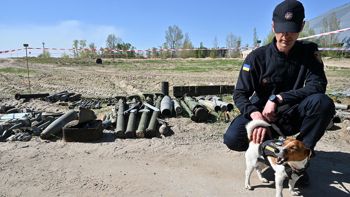 A deminer and his explosive material sniffer dog Patron stand next to unexploded material at an airport in the Kyiv region, on May 5, 2022. (Sergei Supinsky/AFP via Getty Images)
