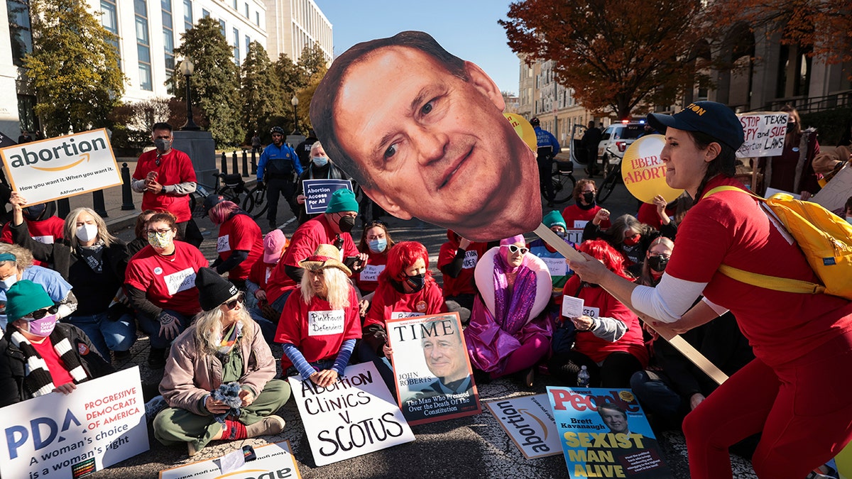 WASHINGTON, DC - DECEMBER 01: An activist with The Center for Popular Democracy Action holds a photo of U.S. Supreme Court justice Samuel Alito as they block an intersection during a demonstration in front of the U.S. Supreme Court on December 01, 2021 in Washington, DC. The Court heard arguments in Dobbs v. Jackson Women's Health, a case about a Mississippi law that bans most abortions after 15 weeks. With the addition of conservative justices to the court by former President Donald Trump, experts believe this could be the most important abortion case in decades and could undermine or overturn Roe v. Wade. (Photo by Chip Somodevilla/Getty Images)