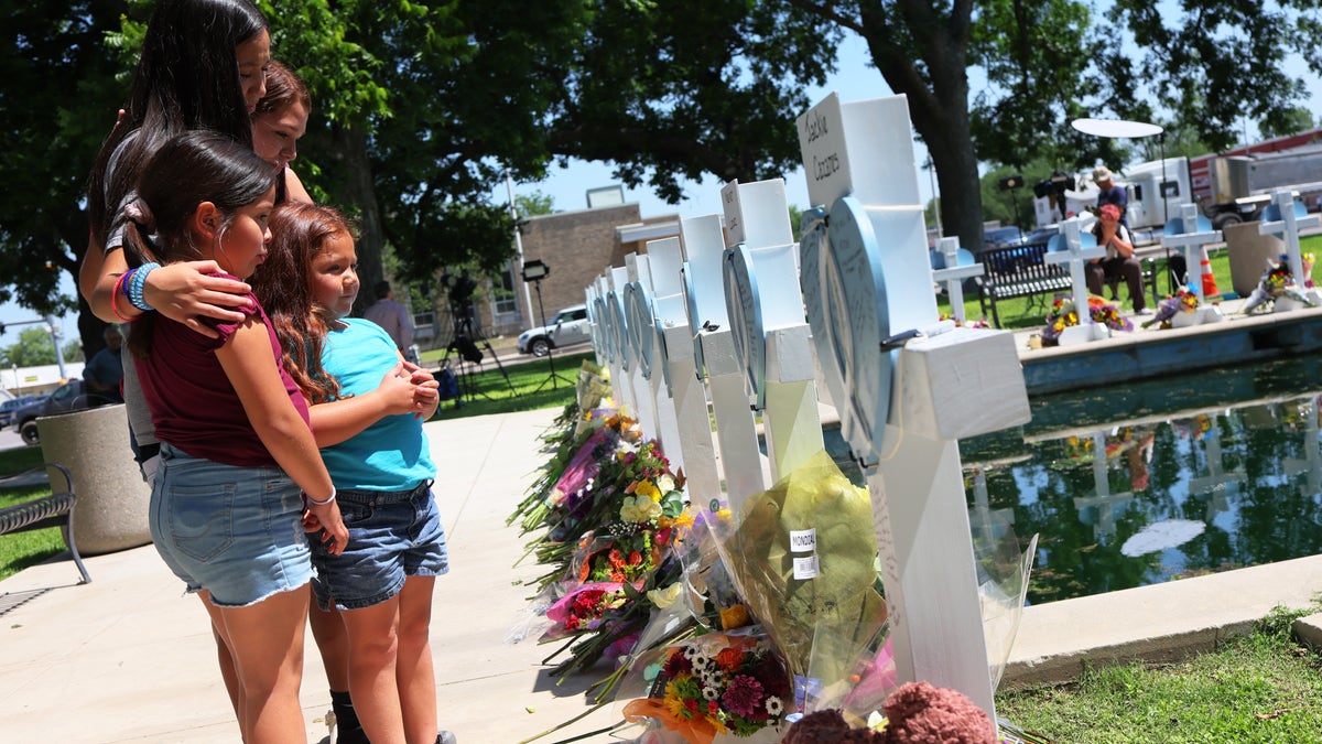 A family stands before a blue and white memorial honoring those lost in a deadly school shooting