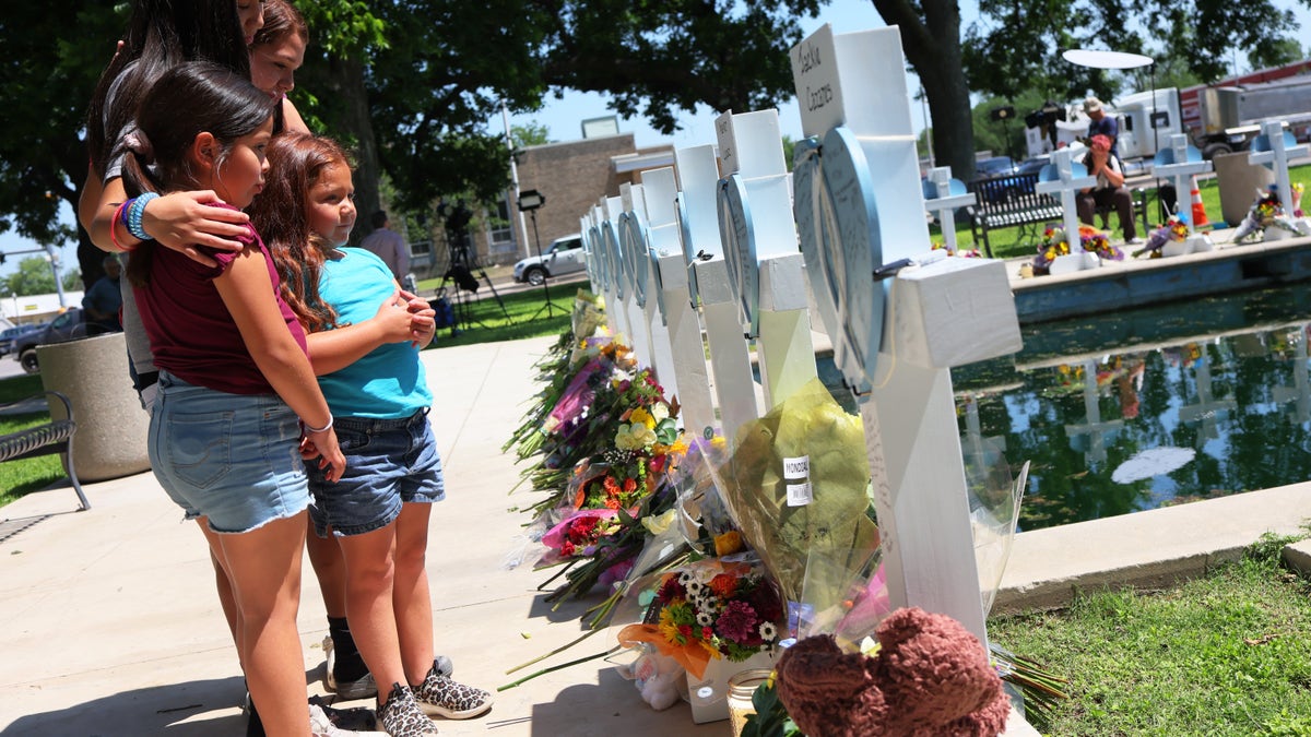 A family stands before a blue and white memorial honoring those lost in a deadly school shooting