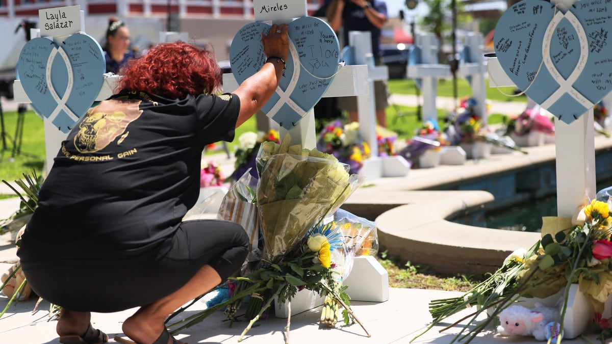 A woman places her hand on top of a memorial in Uvalde