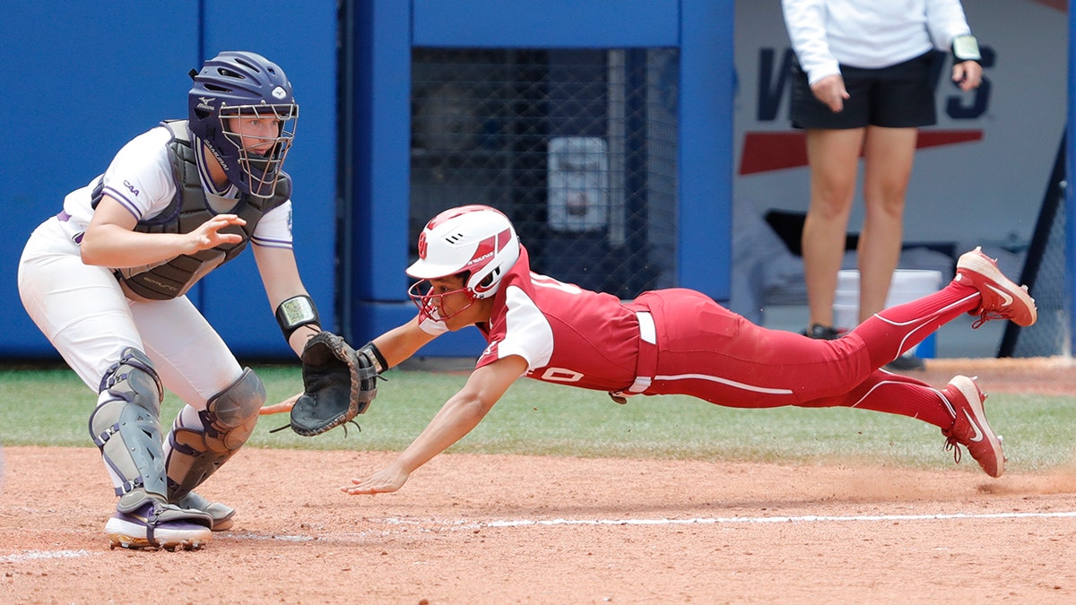 Oklahoma's Rylie Boone (0) slides in at home past James Madison catcher Lauren Bernett (22) to score a run in the sixth inning during a Women's College World Series semi finals game at USA Softball Hall of Fame Stadium. Oklahoma won 6-3.