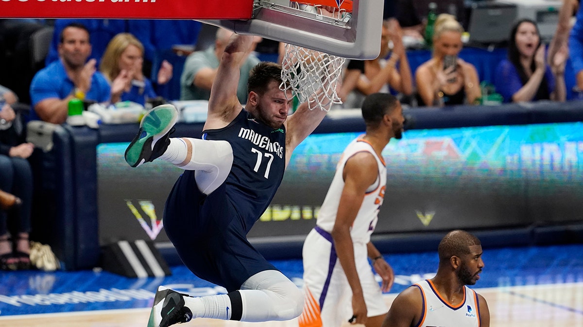Dallas Mavericks guard Luka Doncic (77) hangs on the rim over Phoenix Suns guard Chris Paul, right, after scoring during the second half of Game 6 of an NBA basketball second-round playoff series, Thursday, May 12, 2022, in Dallas.