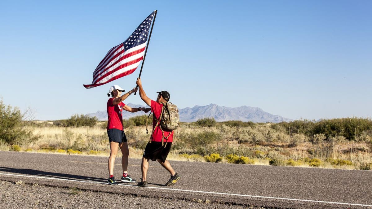 Two men pass an American flag on an open road.