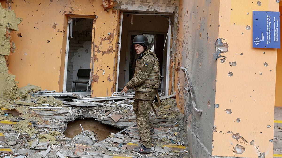 Ukrainian service member wearing fatigues and a helmet stands amid rubble in Luhansk
