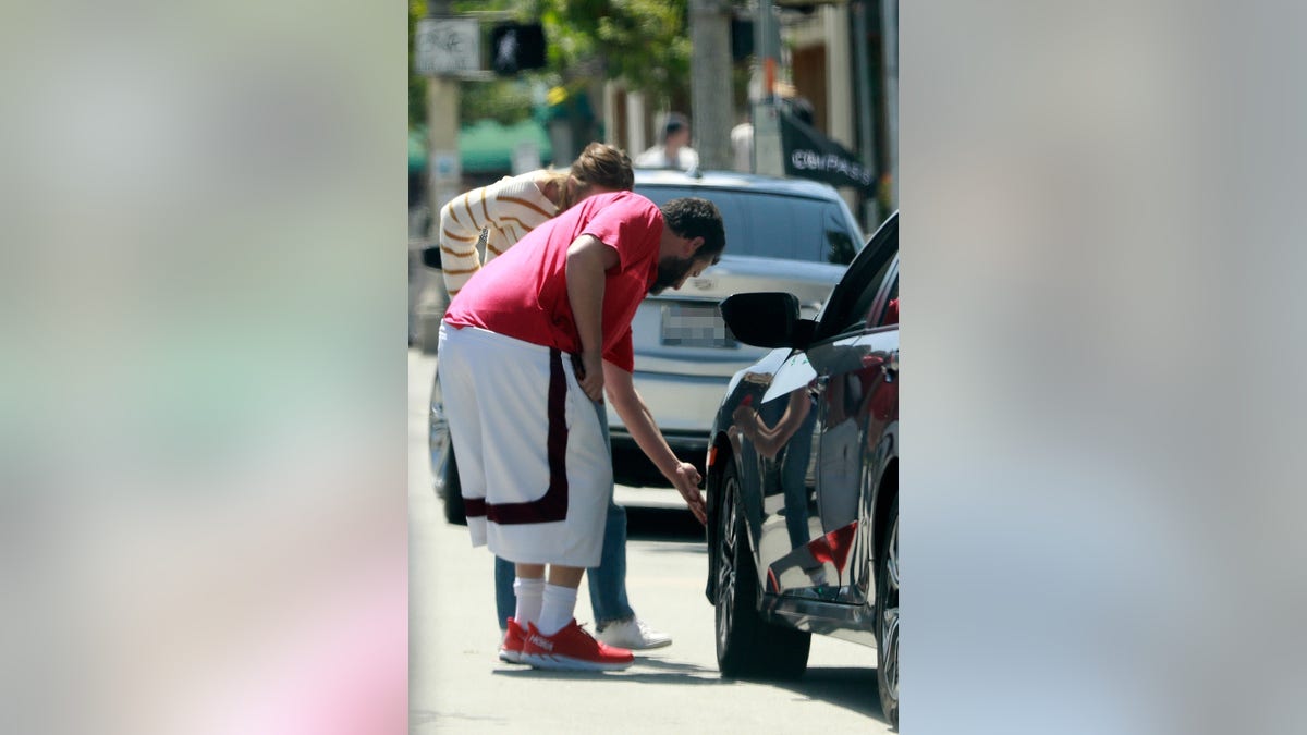 Adam Sandler looked for damages on a car after a crash