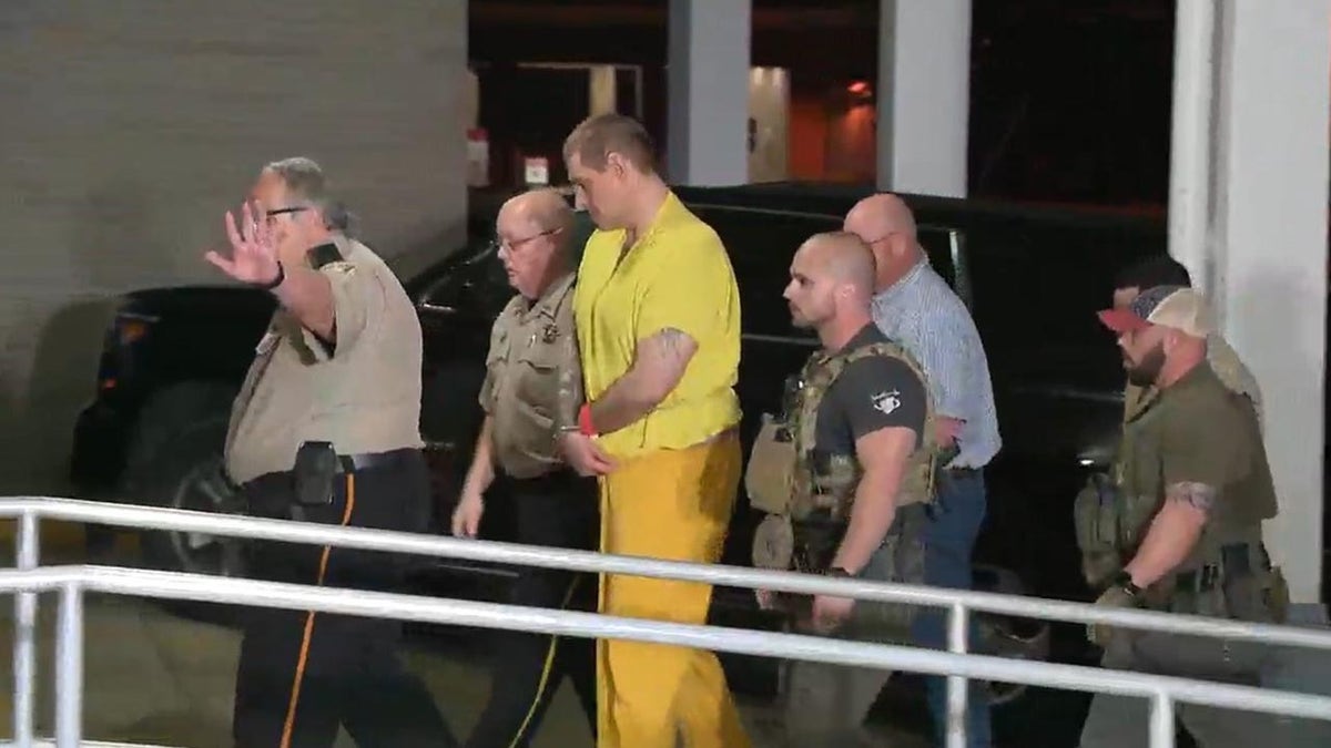 Casey White arrives back in Alabama wearing a yellow jumpsuit and handcuffs