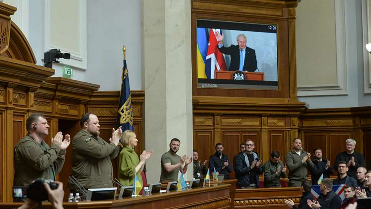 Ukrainian President Volodymyr Zelenskyy, center, applauds as Britain's Prime Minister Boris Johnson, seen on the screen, waves during a session at Ukraine's parliament, in Kyiv, Ukraine on Tuesday, May 3.