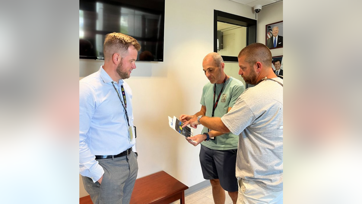 Air Traffic Manager Ryan Warren (left) and controller Robert Morgan (center) show Harrison (far right) printouts of the Cessna 208 flight deck that was used to help him land the plane safely.