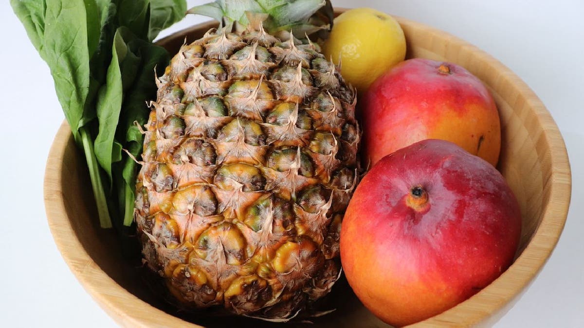 A bowl of spinach, pineapples, mangos and lemons