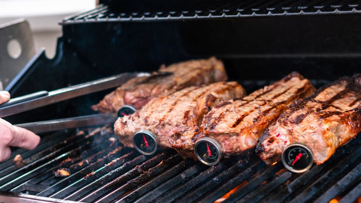 Four steaks with meat thermometers are laid out on a grill