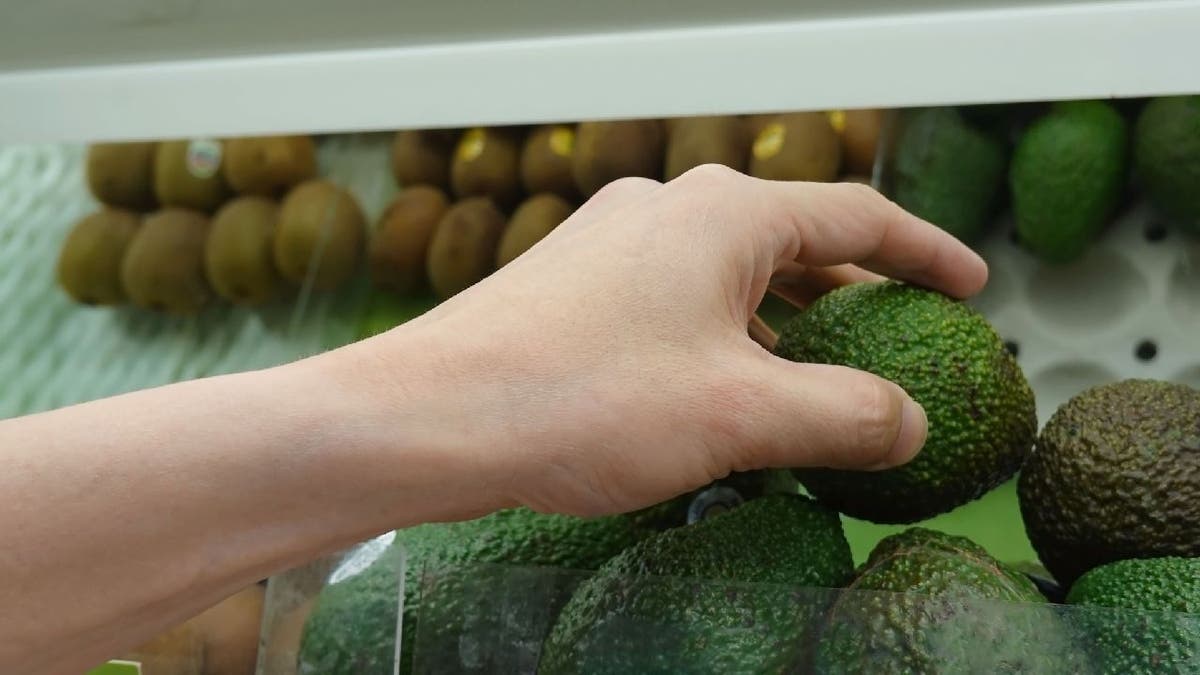 Hand grabs avocado from grocery store shelf