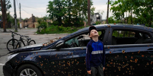 A child standing next to a damaged car looks up at a building destroyed during attacks in Irpin, on the outskirts Kyiv, Ukraine, Monday, May 30, 2022. 