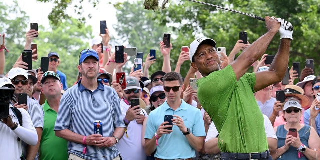 Mark Radetic holds his beer instead of a cellphone as Tiger Woods plays a shot during the PGA Championship on May 20, 2022 in Tulsa, Oklahoma.