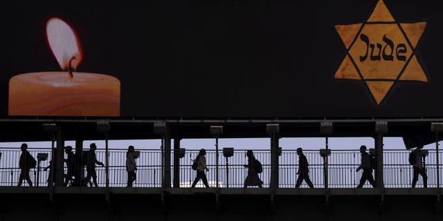 People walk along a bridge under a billboard showing a yellow Star of David, resembling the one Jews were forced to wear in Nazi Germany, on the annual Holocaust Remembrance Day in Ramat Gan, Israel, April 28, 2022.