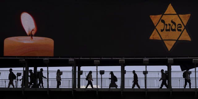 People walk along a bridge under a billboard showing a yellow Star of David, resembling the one Jews were forced to wear in Nazi Germany, on the annual Holocaust Remembrance Day in Ramat Gan, Israel, April 28, 2022.