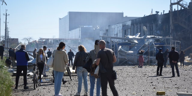 People stand near a destroyed building on the outskirts of Odesa, Ukraine, Tuesday, May 10, 2022. The Ukrainian military said Russian forces fired seven missiles a day earlier from the air at the crucial Black Sea port of Odesa, hitting a shopping center and a warehouse.