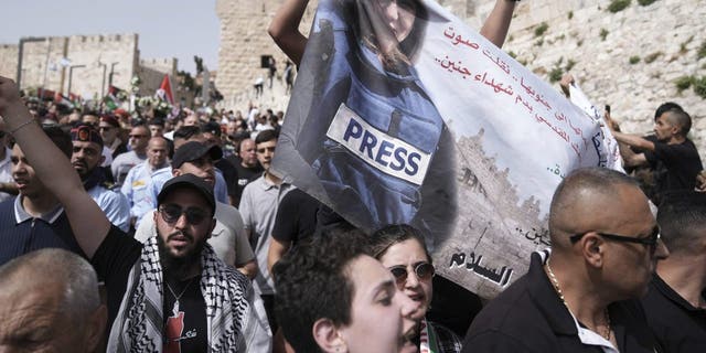 Les personnes en deuil tiennent une bannière représentant Shireen Abu Akleh, journaliste vétéran d'Al Jazeera tuée, alors qu'elles marchent de la vieille ville de Jérusalem à son lieu de sépulture, le vendredi 13 mai 2022. Abu Akleh, un journaliste palestinien-américain qui a couvert le conflit du Moyen-Orient pendant plus de 25 ans, a été abattu mercredi lors d'un raid militaire israélien dans la ville cisjordanienne de Jénine.