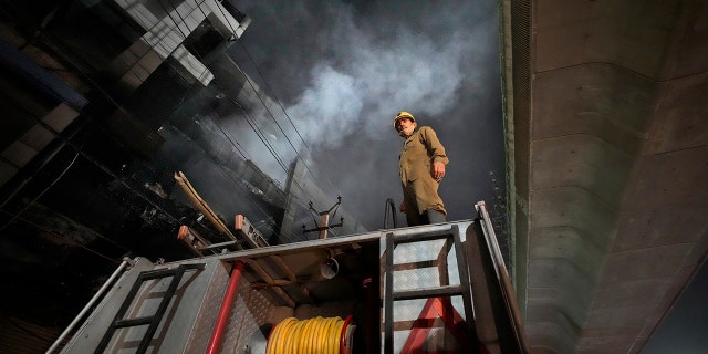 A fire official stands on a fire brigade truck to help his colleagues douse a fire in a four storied building, in New Delhi, India, Saturday, May 14, 2022. A massive fire erupted in a four-storied building in the Indian capital on Friday, killing at least 19 people and leaving several injured, the fire control room said. Dozens of people have been rescued from the commercial building, mainly shops, in the Mundka area in the western part of New Delhi. (AP Photo/Manish Swarup)