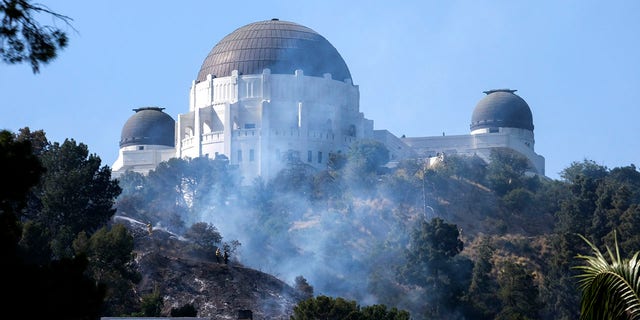 Smoke from a brush fire rises between homes and the Griffith Observatory in the hills of Los Feliz in Los Angeles on Tuesday, May 17, 2022. 