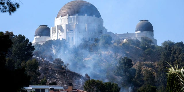 Smoke from a brush fire rises between homes and the Griffith Observatory in the hills of Los Feliz in Los Angeles on Tuesday, May 17, 2022.