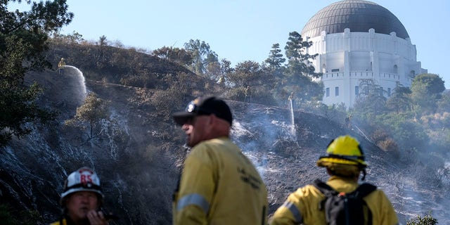 Firefighters spray water on hot spots during a brush fire near the Griffith Observatory in the hills of Los Feliz in Los Angeles on Tuesday, May 17, 2022. 