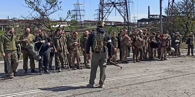 في هذه الصورة المأخوذة من مقطع فيديو نشرته الخدمة الصحفية لوزارة الدفاع الروسية يوم الأربعاء 18 مايو 2022 ، يقف جنود أوكرانيون في جفن جندي روسي بعد مغادرة مصنع آزوفستال للصلب المحاصر في ماريوبول بأوكرانيا.