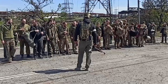 Nesta imagem tirada de um vídeo divulgado pelo serviço de imprensa do Ministério da Defesa da Rússia na quarta-feira, 18 de maio de 2022, soldados ucranianos estão na frente de um soldado russo depois de deixar a siderúrgica Azovstal sitiada em Mariupol, Ucrânia.