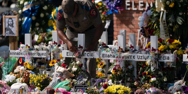 A state trooper places a tiara on a cross honoring Ellie Garcia, one of the victims killed in this week's elementary school shooting in Uvalde, Texas Saturday, May 28, 2022. 