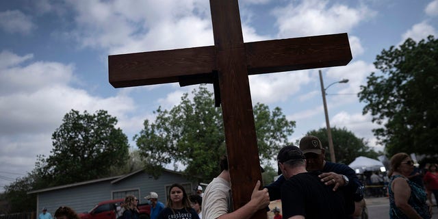 Dan Beazley, right, with his son Joey Beazley, from Detroit, carry a wooden cross on Monday, May 30, 2022, as they pray at a memorial outside Robb Elementary School days after a deadly school shooting in Uvalde, Texas.