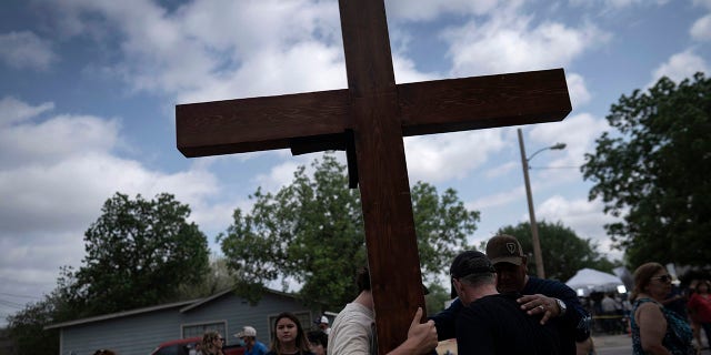 Dan Beazley and his son Joey Beazley, from Detroit, carry a wooden cross as they pray at a memorial outside Robb Elementary School in Uvalde, Texas, Monday, May 30, 2022.