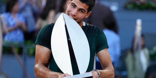 Carlos Alcaraz, of Spain, bites the trophy after winning the final match against Alexander Zverev, of Germany, at the Mutua Madrid Open tennis tournament in Madrid, Spain, Sunday, May 8, 2022.