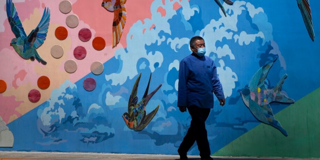 A man wearing a face mask walks past a mural along a street in Beijing, Wednesday, May 25, 2022. 