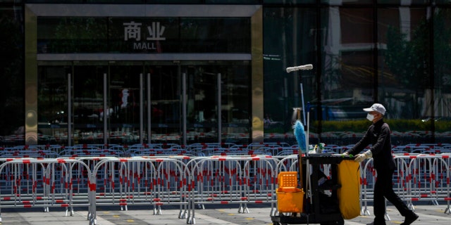 A cleaner wearing a face mask walks by roll of barricades set up for COVID-19 tests outside a closed commercial office building as many office buildings remain under orders to work from home in Beijing, Wednesday, May 25, 2022. 