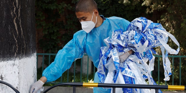 A worker in a hazmat suit removes cordon lines near fences during the coronavirus disease (COVID-19) outbreak in Beijing, China, 25 May 2022.