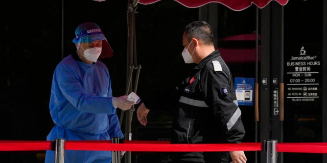 A worker takes the temperature of a resident lining up for mass COVID test on Wednesday, May 11, 2022, in Beijing.