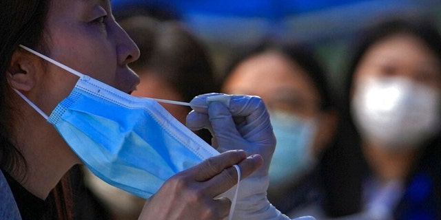 A woman holds her mask as she gets swabbed during a mass COVID testing in the Chaoyang district on Wednesday, May 11, 2022, in Beijing. 