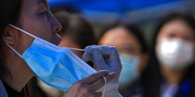 A woman holds her mask as she gets swabbed during a mass COVID testing in the Chaoyang district on Wednesday, May 11, 2022, in Beijing.