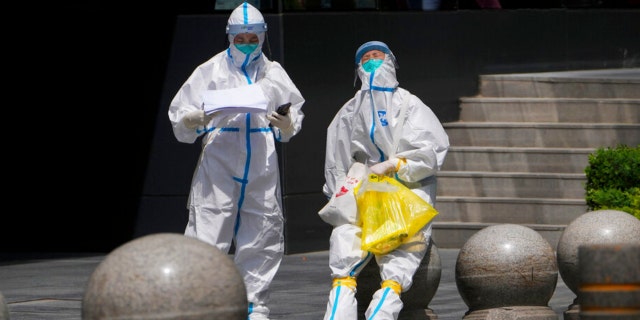 Medical workers in protection suits take a rest after conducting COVID tests for residents near a commercial office complex on Thursdays, May 12, 2022, in Beijing.