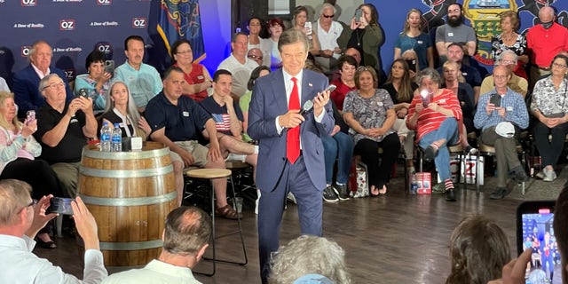 El candidato republicano al Senado, Mehmet Oz, escucha mientras el expresidente Donald Trump llama en el mitin de la víspera de las primarias de Oz en Blue Bell, Pensilvania, el 16 de mayo de 2022