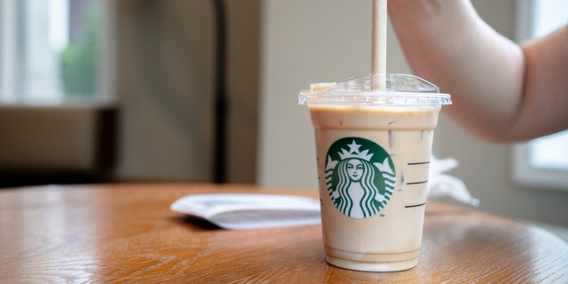 A customer is using a paper straw to drink a cold Starbucks latte.