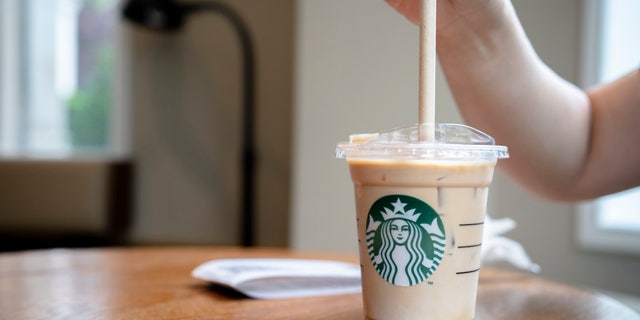A customer is using a paper straw to drink a cold Starbucks latte.