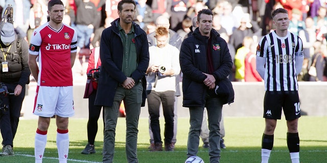 Wrexham owners Ryan Reynolds and Rob McElhenney stand with Wrexham's Ben Tozer (left) and Torquay United's Armani Little (right) during a minute silent for remembrance before the Vanarama National League match at the Racecourse Ground, Wrexham. Picture date: Saturday October 30, 2021.