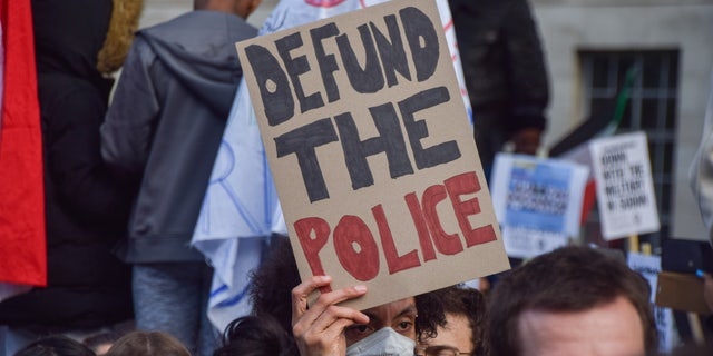 A protester holds a 'Defund The Police' placard.