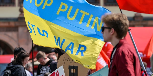 A participant of the central rally of the German Trade Union Confederation (DGB) for Saxony stands in front of a flag "Stop Putin, Stop War" in the colors of Ukraine on the market square in Leipzig on May 1, 2022. 