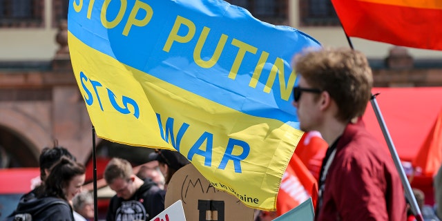 A participant of the central rally of the German Trade Union Confederation (DGB) for Saxony stands in front of a flag "Stop Putin, Stop War" in the colors of Ukraine on the market square in Leipzig on May 1, 2022.