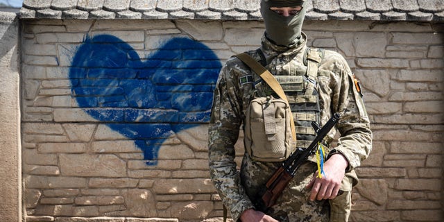 A Ukrainian soldier poses for a photo in front of a wall of heart-shaped graffiti while patrolling an undisclosed location in Kharkiv Oblast.