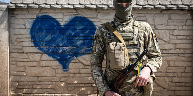 A Ukrainian soldier poses for a photo in front of a wall of heart graffiti during his patrol in an undisclosed location in Kharkiv oblast.