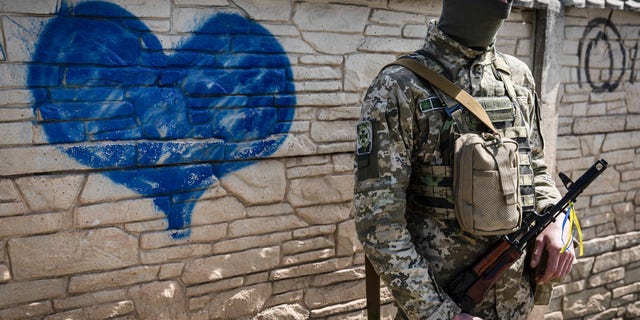 A Ukrainian soldier poses for a photo in front of a wall of heart graffiti during his patrol in an undisclosed location in Kharkiv oblast.